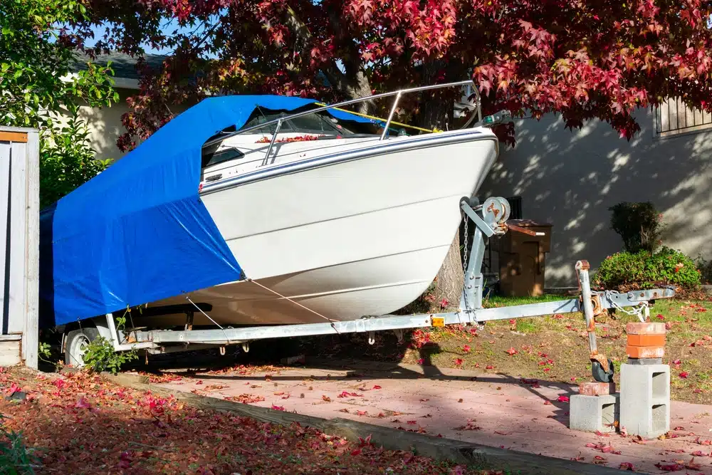 Storing a boat at home on trailer in driveway with blue tarp and cinderblock