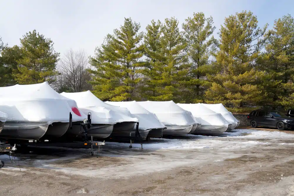 A row of shrink-wrapped and winterized boats stored together in an outdoor boat storage lot.