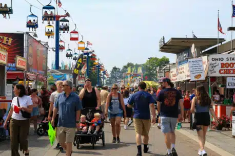 A crowd of people and families walking on midway under the sky gliders at the Ohio State Fair