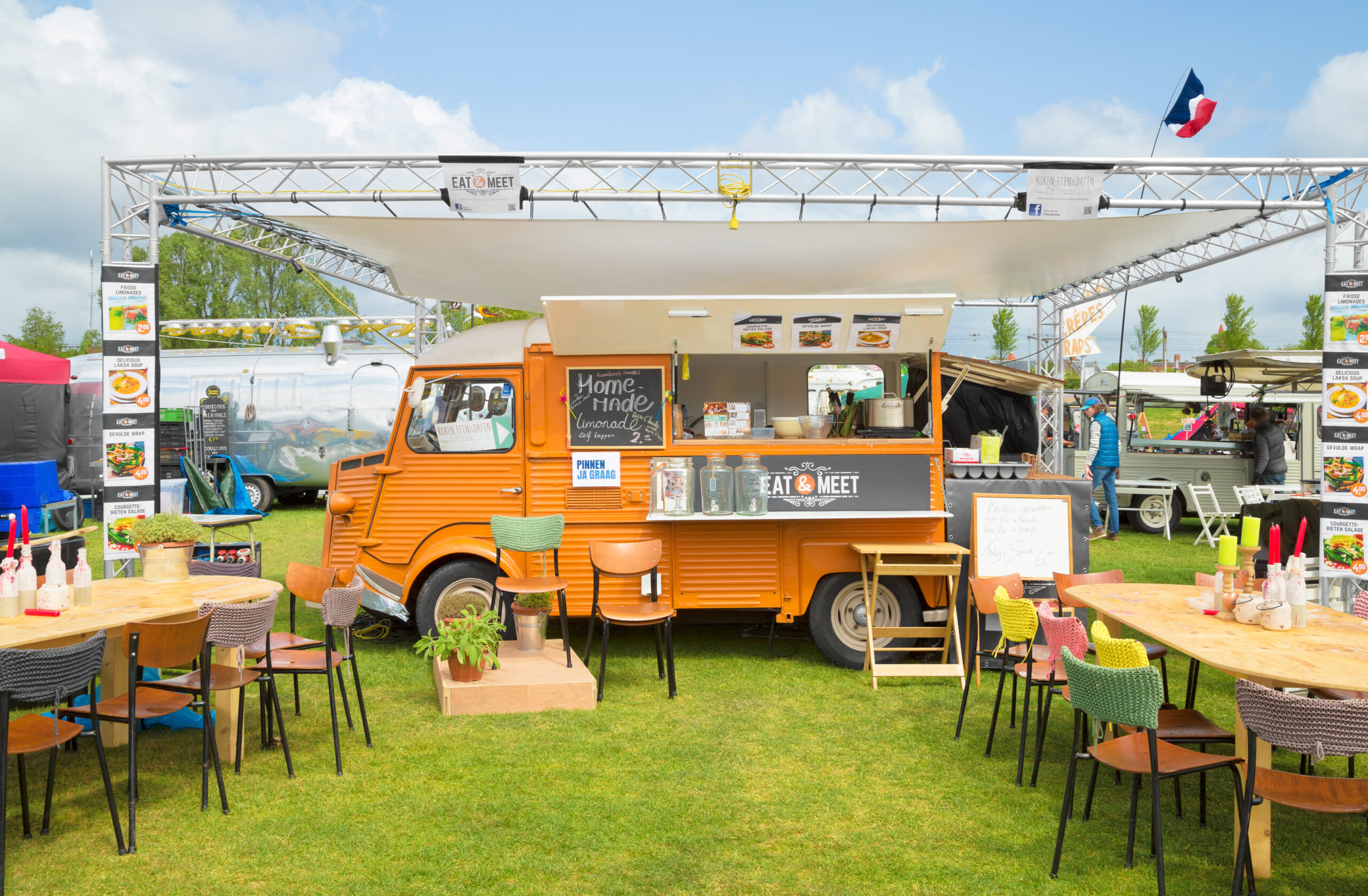 Parked orange food truck with tables and chairs nearby