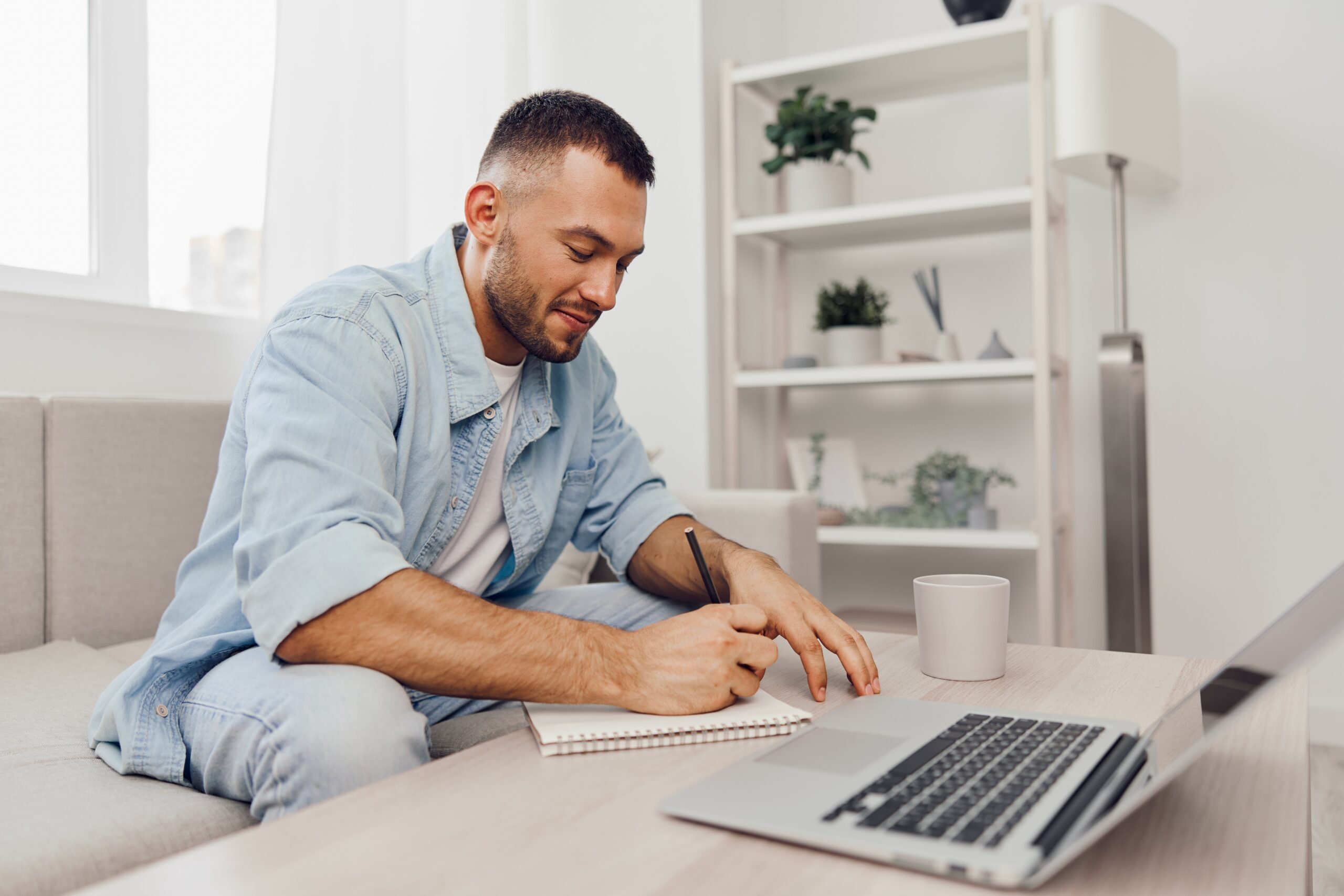 man writing in desk with laptop