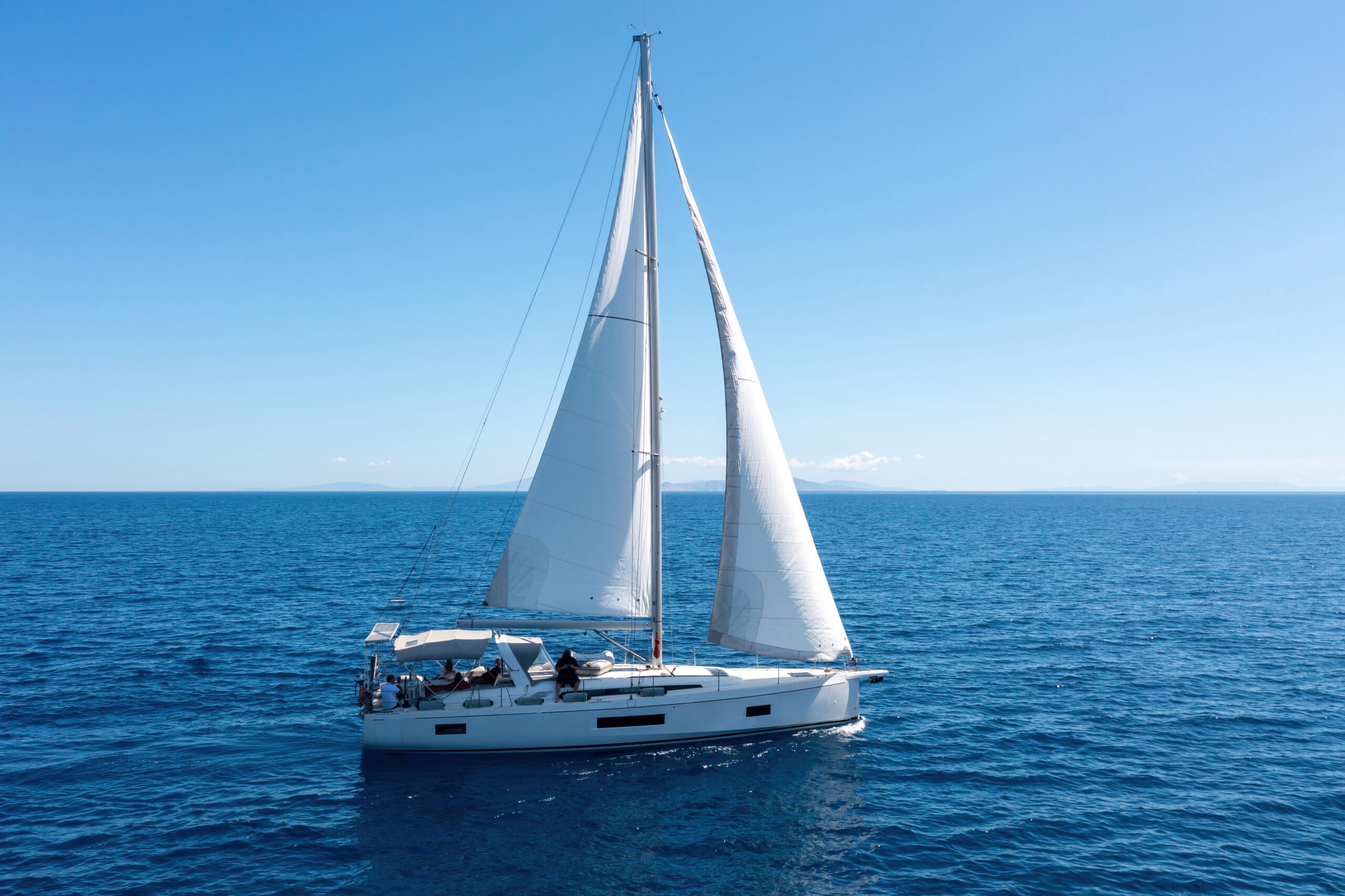 An aerial view of a white sailboat under full sail on deep blue open water on a clear, sunny day, illustrating the wind-powered category within the various major types of boats.